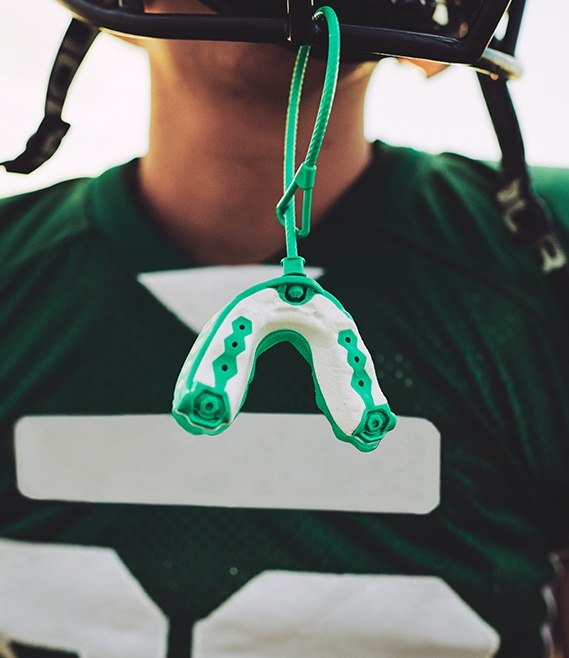 Teen boy with athletic mouthguard hanging from football helmet