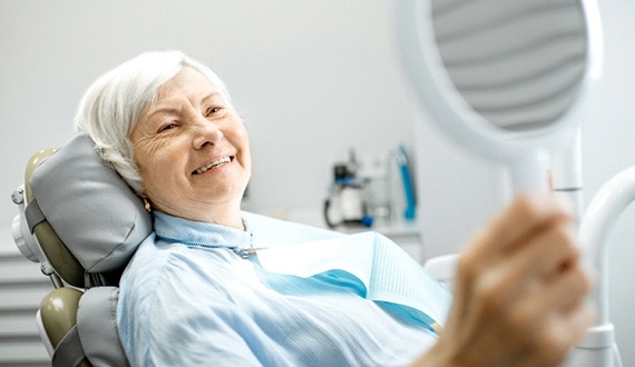 Older woman smiling in dental chair holding mirror