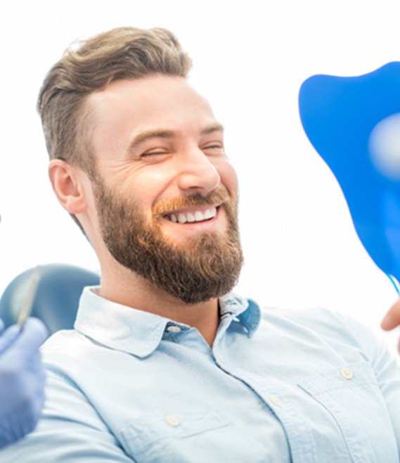 bearded man admiring his new smile in a mirror after a smile makeover in Dallas, TX 