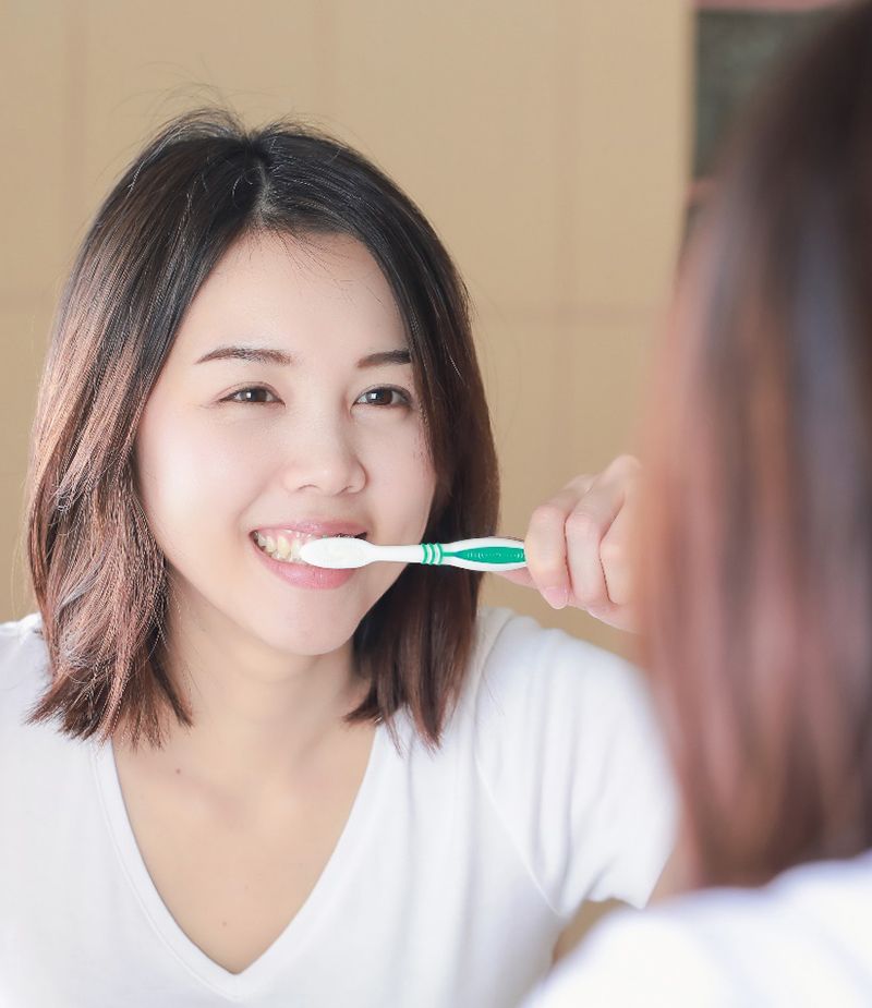 Woman in white shirt brushing her teeth in mirror